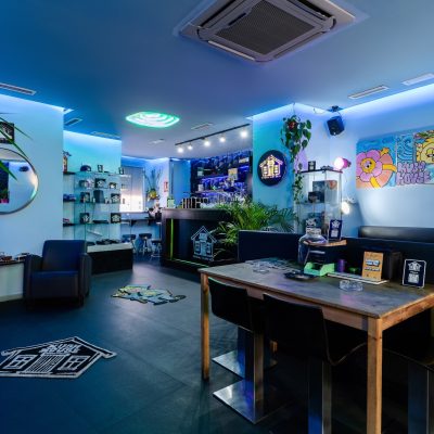 Hlavní místnost Kush House Social Club v Barceloně, se sedačkami, uměleckými díly a modrým osvětlením.