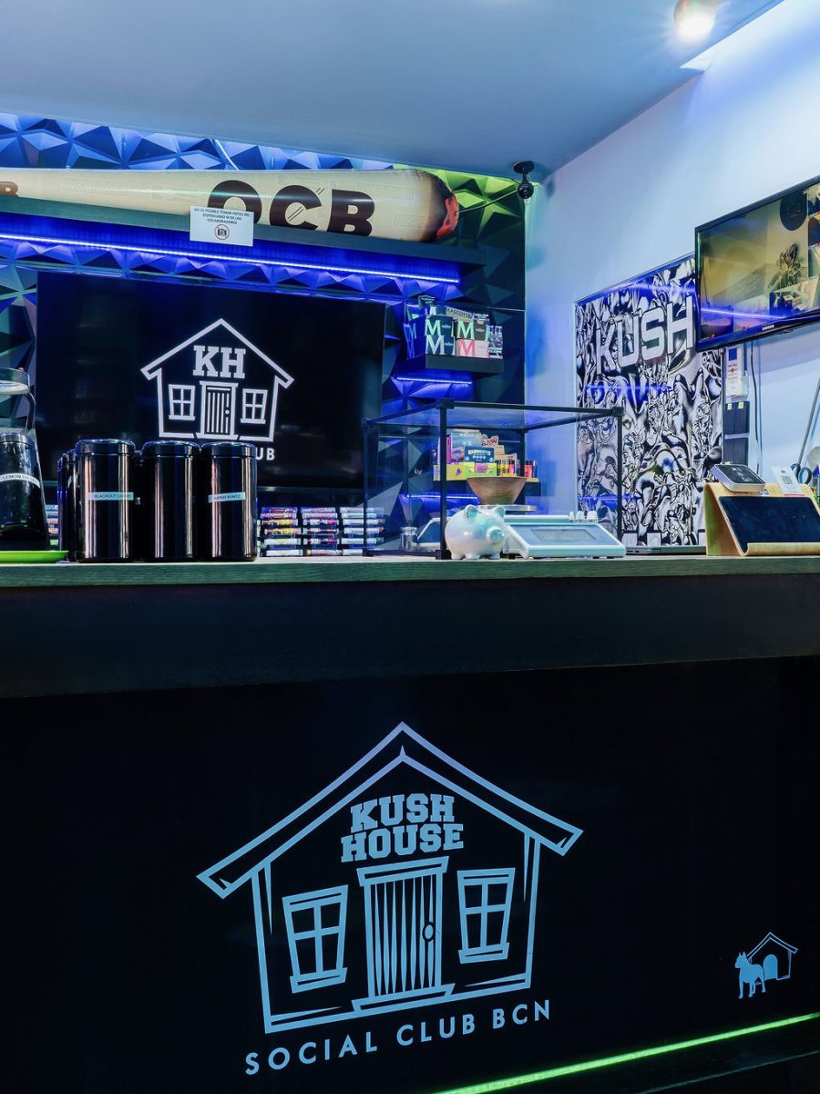 The bar at Kush House Social Club, lit in blue, with the club house logo on the counter front.