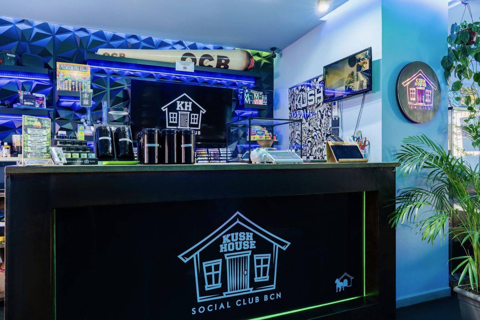 The bar at Kush House Social Club, lit in blue, with the club house logo on the counter front.